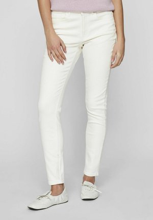 Jeans blancos ajustados de mezclilla, con un diseño clásico de cinco bolsillos. Combinados con zapatillas blancas, mostrando una silueta elegante y entallada.