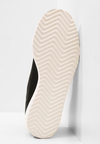 Black sneaker sole featuring a textured white rubber outsole with a zigzag tread pattern and a smooth black leather upper.