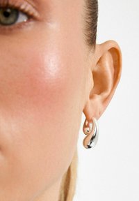 Boucles d'oreilles en argent avec une forme fluide en goutte d'eau, une surface texturée et un petit accent sphérique. Vue en gros plan de l'oreille et de la boucle d'oreille.
