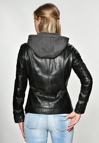 Svart läderjacka med en grå hoodie, figursydd design, slät textur och tryckknappdetaljer. Har sömsyning och kontrasterande material.