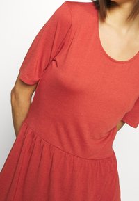Rotes, kurzärmliges Kleid mit rundem Ausschnitt, gerafftem Taillenbereich und ausgestellt Rock. Hergestellt aus einem weichen, glatten Stoff mit gleichmäßiger Textur.