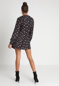 Černé šaty s dlouhými rukávy, malé růžové květinové vzory, zúžený pas, rozšířená sukně, nošeny s černými kotníkovými botami.