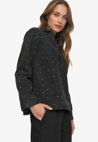 Chemise en velours côtelé noir avec des éclats blancs, à manches longues, col classique et coupe décontractée. Tissu texturé et détail de patte de boutonnage cachée.