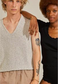 Twee personen staan naast elkaar. De man draagt een lichtgrijs, gestructureerd mouwloos shirt met een V-hals; de vrouw draagt een aangesloten zwart shirt met korte mouwen en een gekartelde rand.