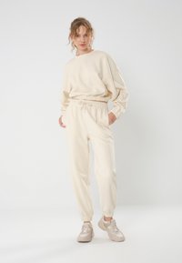 Cremfarbene Sportbekleidungsset bestehend aus einem lässigen Sweatshirt mit überschnittenen Schultern und passenden Jogginghosen mit elastischem Bund und Taschen.