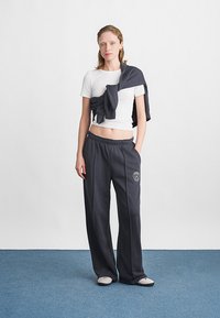 Biała koszula z krótkim rękawem i ciemnoszare dresy z elastycznym paskiem. Bluza zarzucona na ramionach. Buty wsuwane. Gładka faktura materiału.