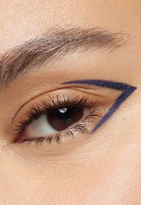 Nærbillede af et øje med et dristigt, vinkelret blåt eyeliner-mønster. Huden fremstår glat med veldefinerede vipper og en naturlig øjenbrynsform.