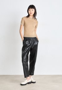 Καφέ κοντομάνικο πουλόβερ με διακριτό σχέδιο ρόμβου, συνδυασμένο με κομμένα μαύρα δερμάτινα παντελόνια και κρέμα μπαλαρίνες με χοντρή μαύρη σόλα.