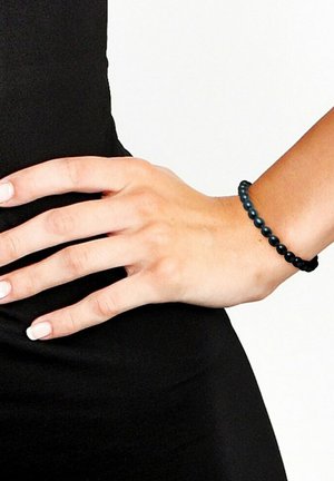 Bracelet en perles noires composé de perles rondes et lisses, avec un design extensible. Porté sur une main sur un fond noir.
