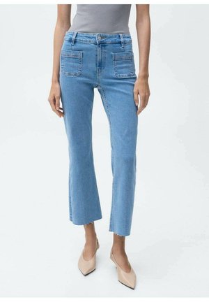Vrouw draagt lichtblauwe cropped flare jeans met voorzakken, een grijs mouwloos topje en beige puntige hakken.