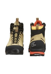 Botas de senderismo con parte superior de ante marrón, puntera de goma negra, cordones dorados, acentos naranjas y suela Michelin para tracción.