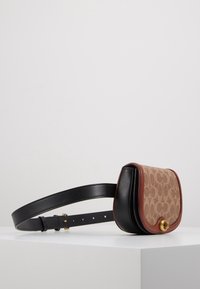 Brun mønstret stof og en sort læder crossover-taske med detaljer i guldhardware, kurvet form og justerbar sort rem.