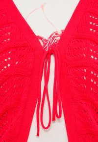 Πλεκτή κόκκινη ζακέτα με V λαιμόκοψη, διακοσμητικά σχέδια ανοιχτού πλέγματος και κορδόνι για κλείσιμο μπροστά. Ελαφριά, σχεδιασμένη για στρώση.