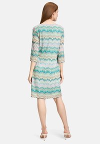 Kleid mit Dreiviertelärmeln, das ein Zickzackmuster in Tönen von Teal, Beige und Weiß zeigt. Der Stoff wirkt leicht und hat eine glatte Textur.