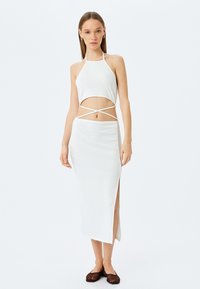 Weißes geripptes Zweiteiler-Set mit einem Top im Halter-Neck-Stil und Ausschnitten sowie einem langen Rock mit einem seitlichen Schlitz. Akzentuiert mit dünnen Trägern und einem figurbetonten Design.