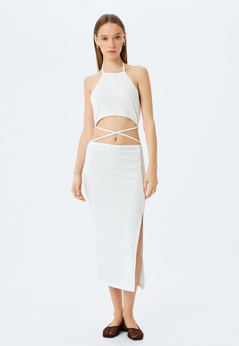 Weißes geripptes Zweiteiler-Set mit einem Top im Halter-Neck-Stil und Ausschnitten sowie einem langen Rock mit einem seitlichen Schlitz. Akzentuiert mit dünnen Trägern und einem figurbetonten Design.