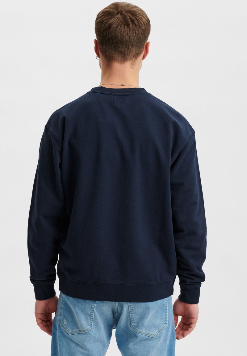 Navy blauwe sweatshirt met lange mouwen, ronde hals en geribbelde manchetten en zoom. De stof lijkt zacht en heeft een licht gestructureerde achterkant.