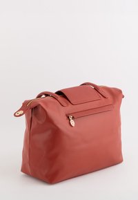 Grand sac à main en cuir rouge doux avec doubles poignées, fermeture à glissière sur le dessus et petite poche zippée à l'avant avec un tirant en forme de feuille.