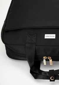 Bolso acolchado negro hecho de nailon con tiradores de cremallera dorados. Presenta una etiqueta 'Wittchen' y asas de tela resistentes para facilitar el transporte.
