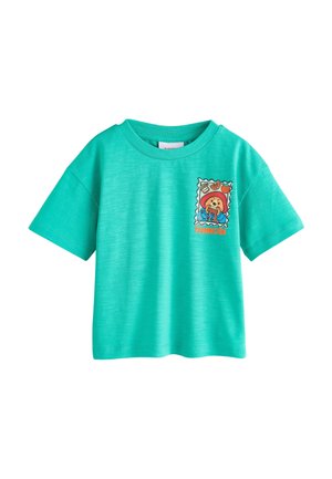 Tyrkysové tričko s krátkým rukávem s grafikou razítka Medvídka Paddingtona, který jí sendvič, na levé straně hrudi.