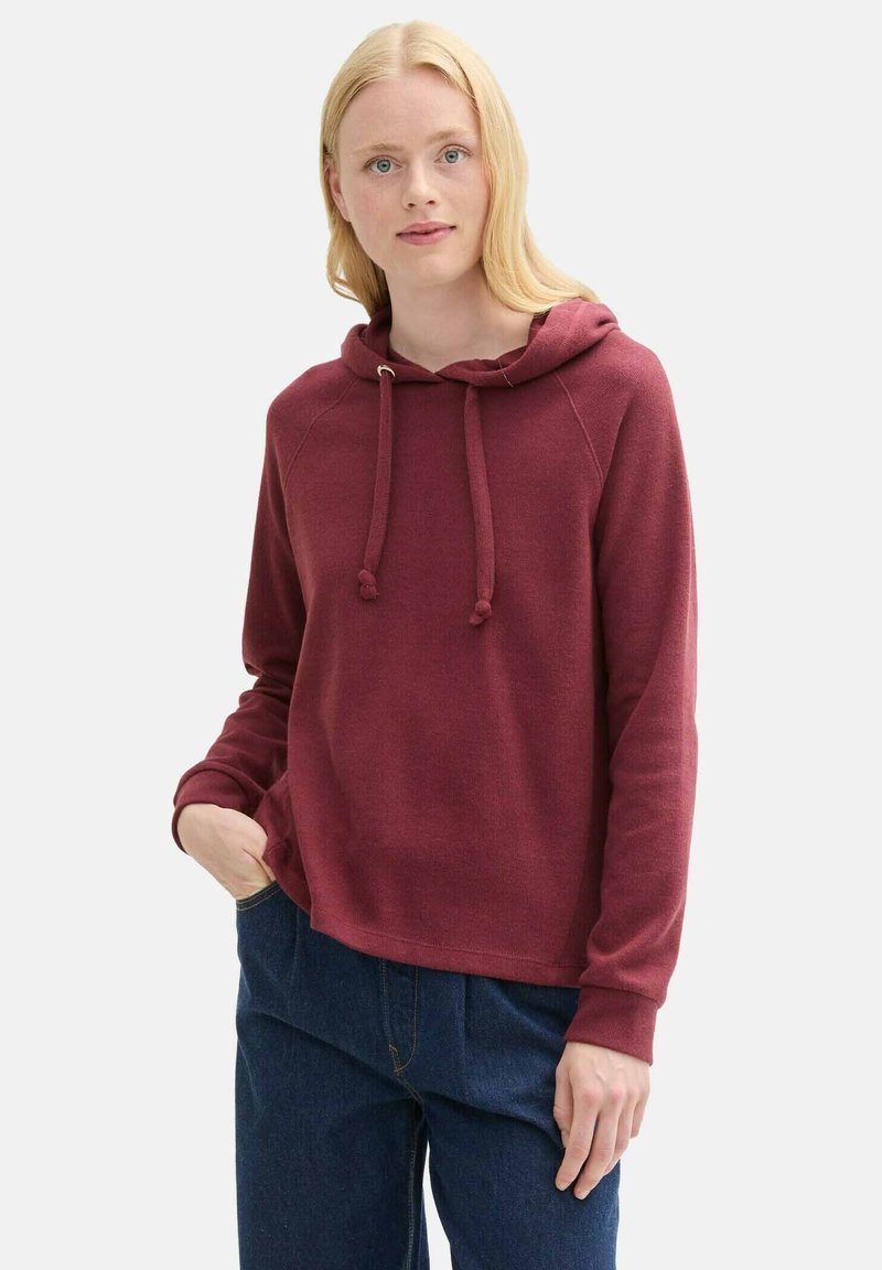 Brūns kapuces džemperis ar brīvu piegriezumu, auklām un ribotām aprocēm. Apvienots ar vaļīgām zilām džinsu biksēm. Gluda tekstūra.