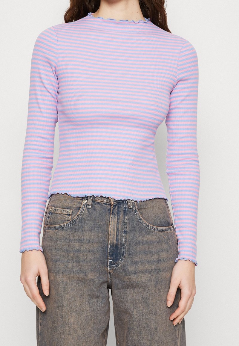 Bluzka z długim rękawem w jasnofioletowe i różowe paski, z ozdobnym dekoltem i falistym dołem. W zestawie z wysokim stanem jeansami w niebieskim kolorze.