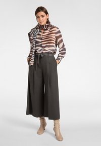 Blusa a strisce multicolore con maniche lunghe, pantaloni a palazzo grigio scuro e stivali con tacco color beige chiaro, abbinati a una sciarpa coordinata.
