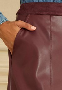 Bordeauxfarbenen Lederrock mit einem Wildlederbund und seitlicher Tasche, mit glatter Textur und sichtbaren Nähten für zusätzliche Details.