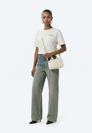 Nő fehér Diesel pólóban, kifakult, bőszárú farmerral, fekete hegyes orrú magassarkúval, ezüst karikafülékkel, és egy kis fehér keresztpántos táskával.