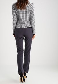 Svartvit houndstooth-mönstrad åtsittande tröja, i kombination med marinblå byxor och svarta högklackade skor. Slät textur och skräddarsydd passform.