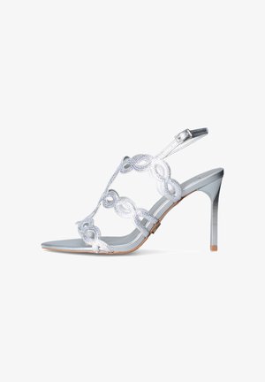 Sandalo argentato con tacco alto, con cinturini decorativi a boucle e fibbia alla caviglia, tacco a stiletto sottile e punta aperta.