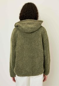 Veste en polaire verte avec une surface texturée, capuche et coupe ample. Caractéristiques des épaules tombantes et des manches longues, conçue pour la chaleur.