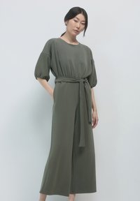 Giubbotto verde oliva realizzato in tessuto morbido, con scollatura rotonda, maniche corte a sbuffo e una cintura coordinata in vita.