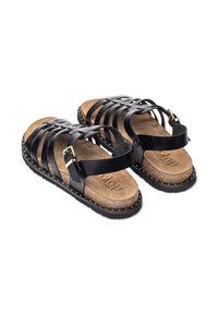 Sandalias de tiras de cuero negro con plantilla de corcho, hebilla dorada y detalle de tachuelas en suelas de goma negra, mostradas una al lado de la otra sobre un fondo blanco.