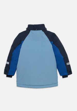 Veste d’hiver longue bleu et marine avec un dos bleu clair, des manches bleu foncé et des patchs réfléchissants sur le bas des bras, vue de dos.