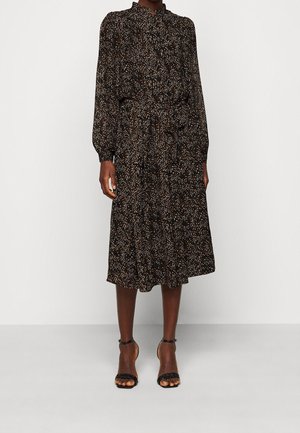 Robe midi noire avec un motif floral blanc et rouille. Manches longues, col montant, taille cintrée et jupe évasée. Portée avec des sandales noires à talons.