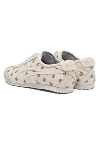 Baskets en cuir blanc avec de petits motifs cartoon, détails texturés, fermeture à lacets sur le devant et semelle extérieure en caoutchouc. Marque "Tiger" sur les languettes arrière.