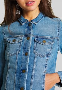 Denim jacket in light blue with a classic fit, button-up front, two chest pockets, and rounded collar; features copper-tone buttons.