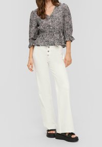 Blusa a maniche puff nere e rosa a fantasia abbinata a pantaloni bianchi a gamba larga con chiusura a bottone e sandali platform neri.