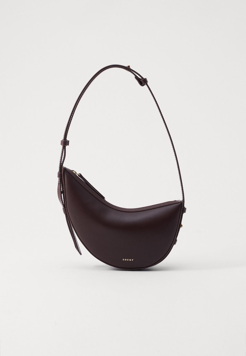 Brown leather crossbody bag with a crescent shape, adjustable strap, and gold hardware detail. Smooth texture, minimalistic design.