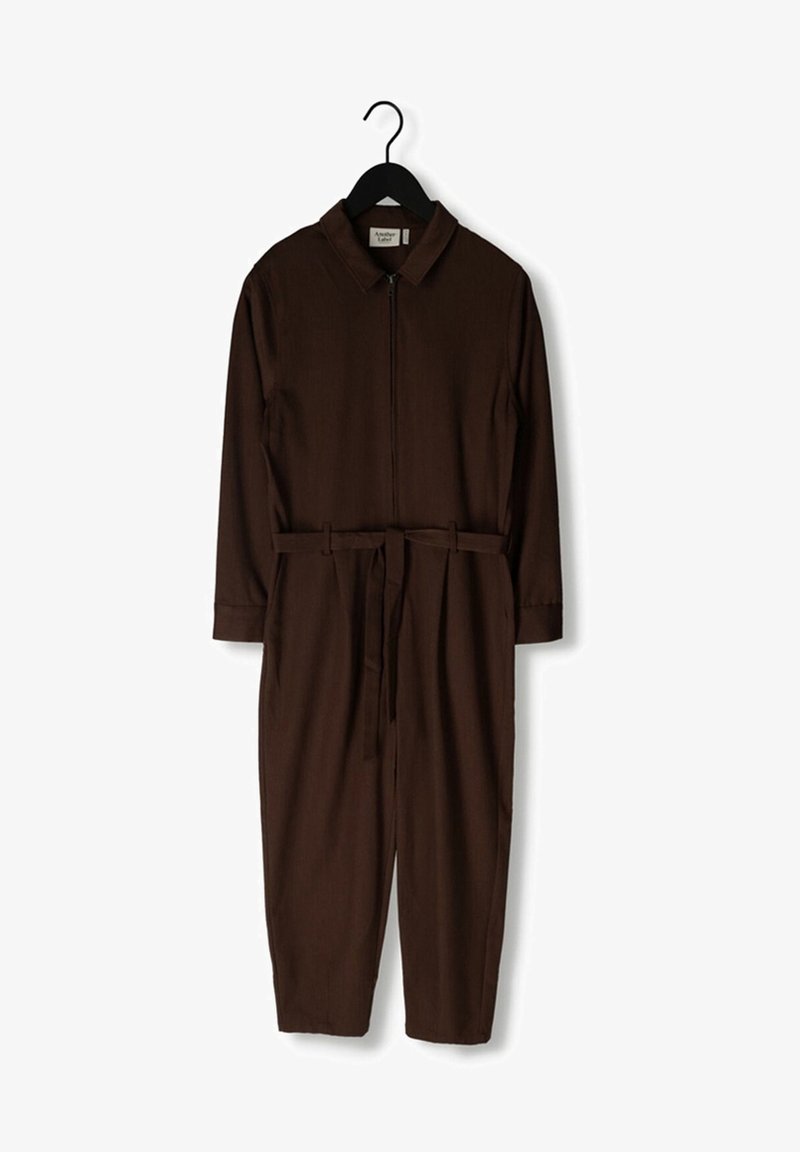 Combinaison marron à manches longues avec col, fermeture éclair frontale, ceinture assortie à la taille, suspendue à un cintre noir sur fond blanc.