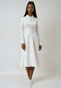 Robe blanche à manches longues avec un col, des rayures verticales, une taille cintrée et une jupe évasée. Portée avec des baskets blanches pour un look décontracté.