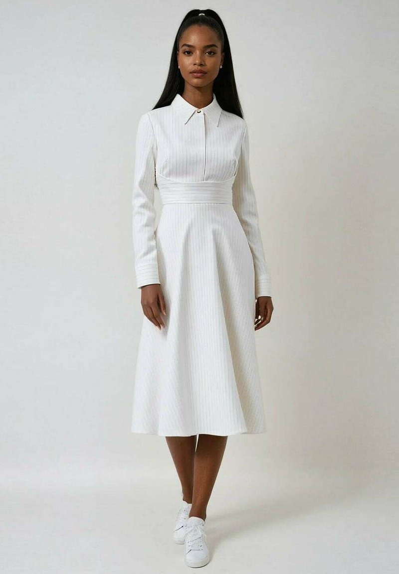 Robe blanche à manches longues avec un col, des rayures verticales, une taille cintrée et une jupe évasée. Portée avec des baskets blanches pour un look décontracté.