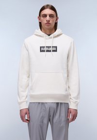 Sudadera blanca con bolsillo frontal, capucha con cordón y logo gráfico negro. Textura de tela lisa, puños y dobladillo acanalados. Combinada con pantalones cargo grises.