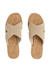 Sandales beiges avec une sangle en tissu perforé en forme de X et une semelle en similicuir texturée, présentant un logo en forme de cœur embossé sur la semelle intérieure.