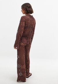 Brązowy strój z szydełkowania z długim rękawem i luźnymi spodniami, prezentujący kwiatowe wzory, ażurowe detale i fakturowane wykończenie.