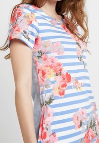 Cotton t-shirt with horizontal blue and white stripes. Features pink and coral floral patterns along the sides. Crew neck and short sleeves.
