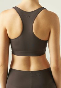 Brun sport-bh med racerback-design, som har slät tyg och minimal sömnad. Logotyp på baksidan, i kombination med matchande högmidjade underdelar.