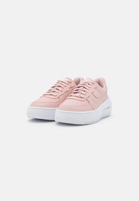 Pink leather sneakers with white rubber soles, textured detailing, and perforations on the toe. Laces secured with a rounded tongue.