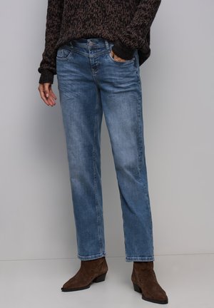 Jasnoniebieskie dżinsy z prostymi nogawkami, z pięcioma kieszeniami i subtelnym wyblaknięciem, zestawione z brązowymi botkami za kostkę.